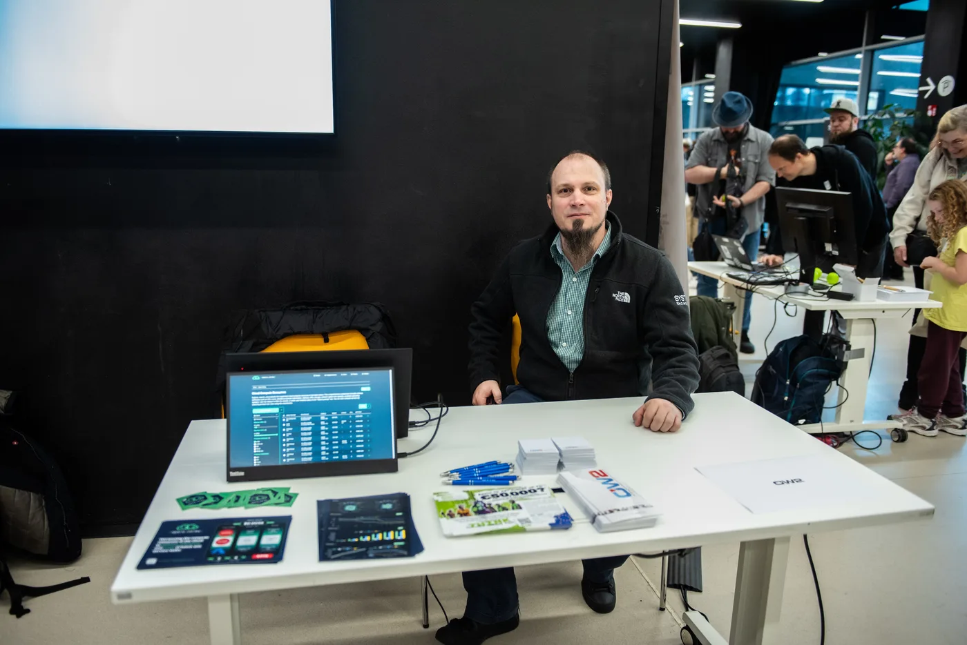 Photo of Gergely Daroczi sitting at the Spare Cores booth (table) at SFSCon 2024 in Bolzano, Italy.